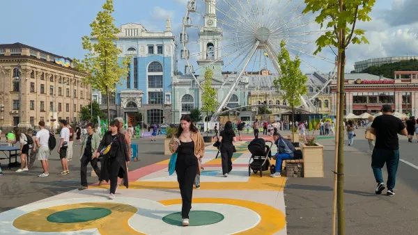 People walking in crowded square in Kyiv, Ukraine with ferris wheel and old buildings.