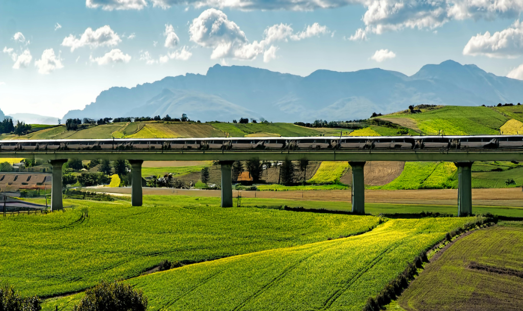 Image of green rolling fields with high-speed rail train passing on elevated rail.