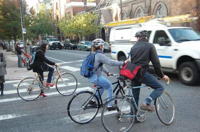 People on bike wearing helmets stopped at intersection waiting for passing cars in Philadelphia, Pennsylvania.