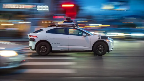 White Waymo autonomous car driving fast down city street with blurred background at night.