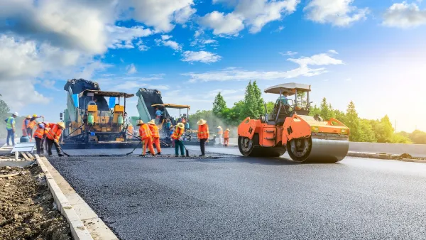 Orange and black heavy equipment and workers building new asphalt roadway.