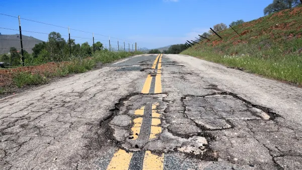 Close-up of cracked and damaged two-lane roadway with double yellow stripes on a bright sunny day.