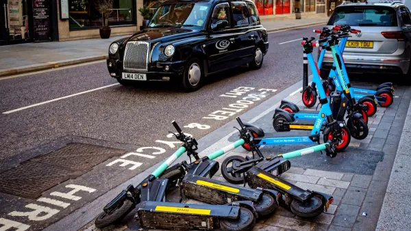 Group of e-scooters messily parked on street in London with black cab in background.