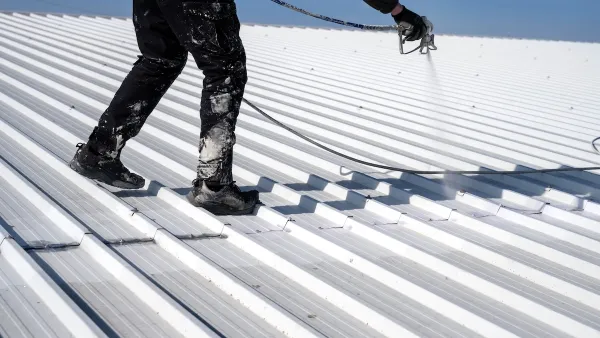 Worker painting metal roof white.