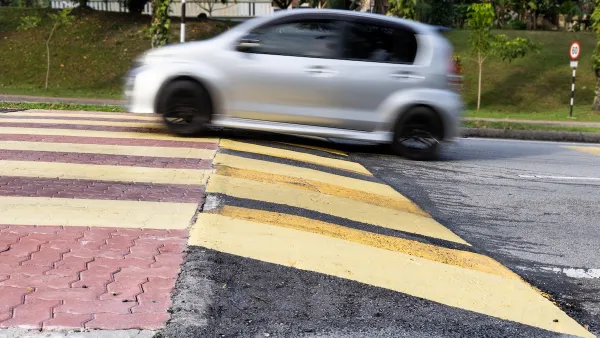 Small silver car driving over wide soeed cushion on asphalt road.