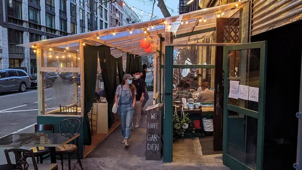 Person wearing mask walking through temporary outdoor dining setup lined with bistro lights at dusk in New York City.