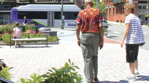 Two people walking away from camera through pedestrian plaza in street in Richmond, Virginia with purple and white city bus moving in background.